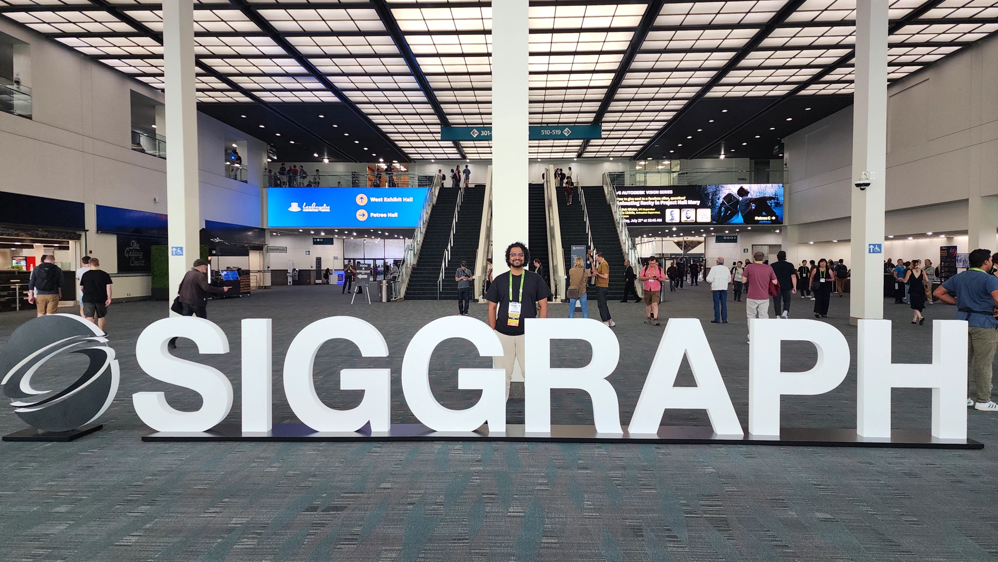 Arjun standing behind large white SIGGRAPH letters inside a convention center.